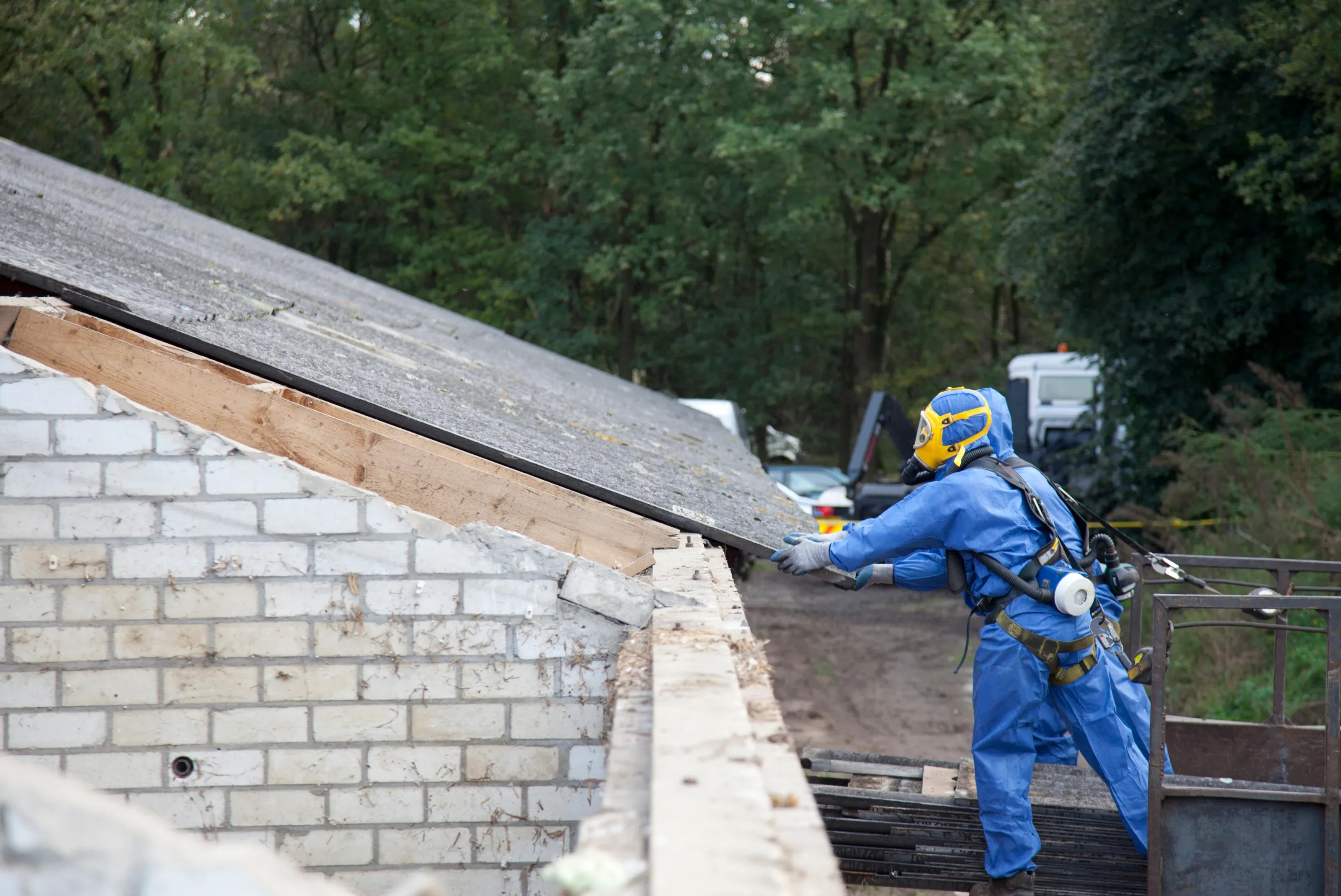 Licensed contractor performing asbestos roof removal with safety equipment